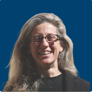 Eleonora Barone sonriendo, con gafas y vestida con ropa oscura, frente a un fondo azul.