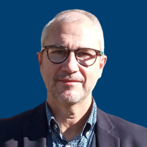 Ignacio Chato con gafas y vestido con traje oscuro, frente a un fondo azul.